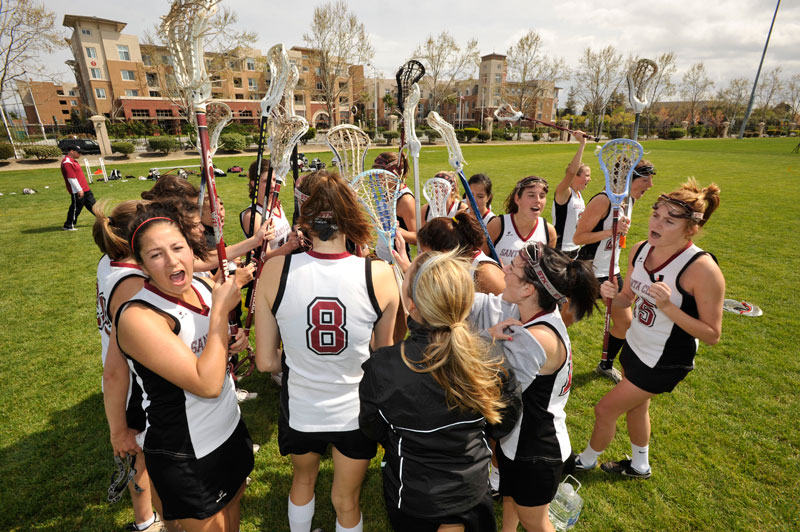 A womens lacrosse team huddles on a grassy field.