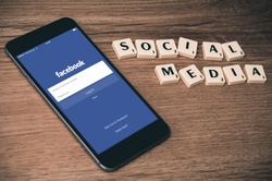 Phone displaying social media login screen and Scrabble tiles spelling Social Media Guidelines.