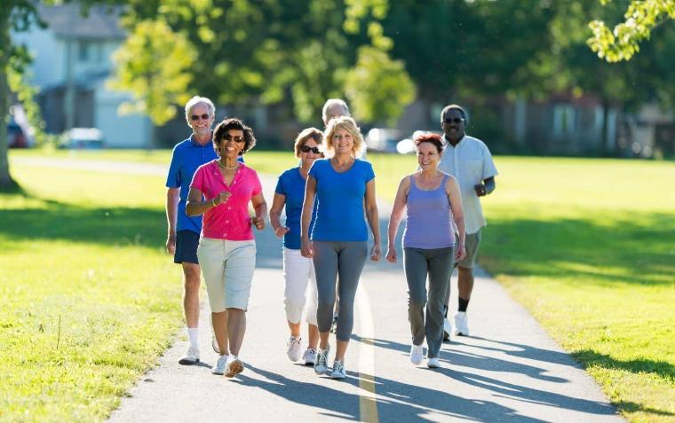 A group of people walking on a sidewalk with grass and trees behind them