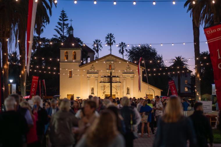 Crowd of alumni mingling in front of the Mission Church at dusk