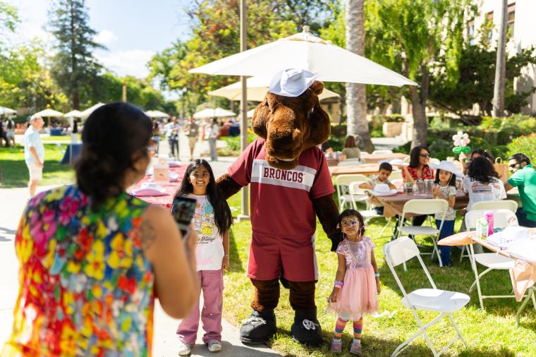 SCU Mascot, Bucky posing for a photo with two children with other event guests in the background
