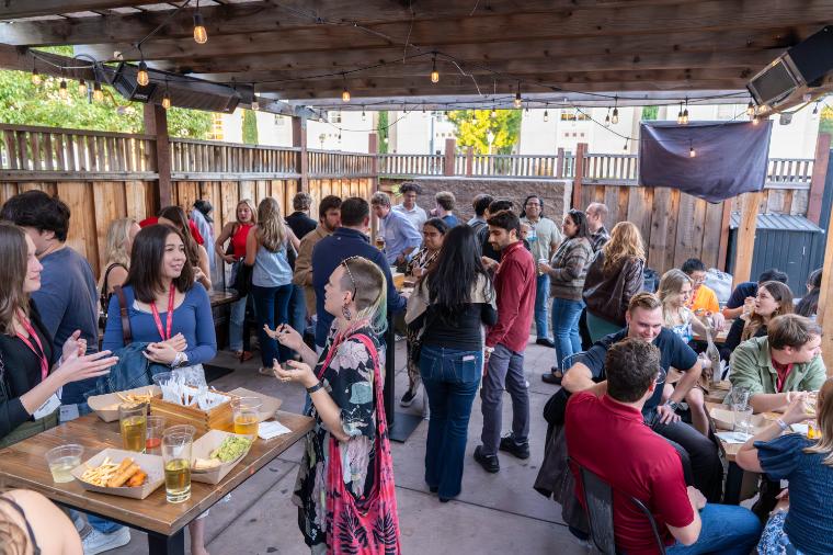 Young alumni talking, eating, and drinking on the patio at The Hut