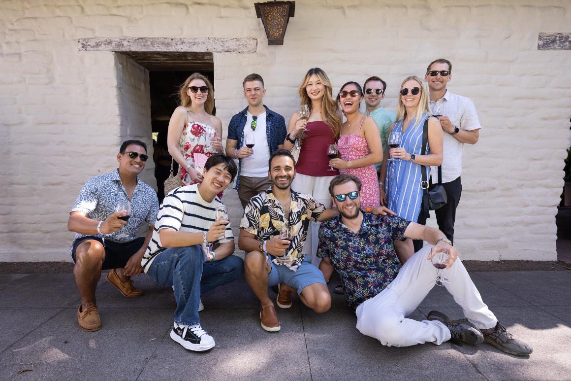 A large group smiles with wine glasses in front of the Adobe Wall