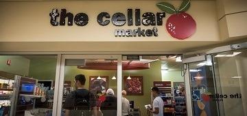 Customers entering a store with a sign that reads The Cellar Market.