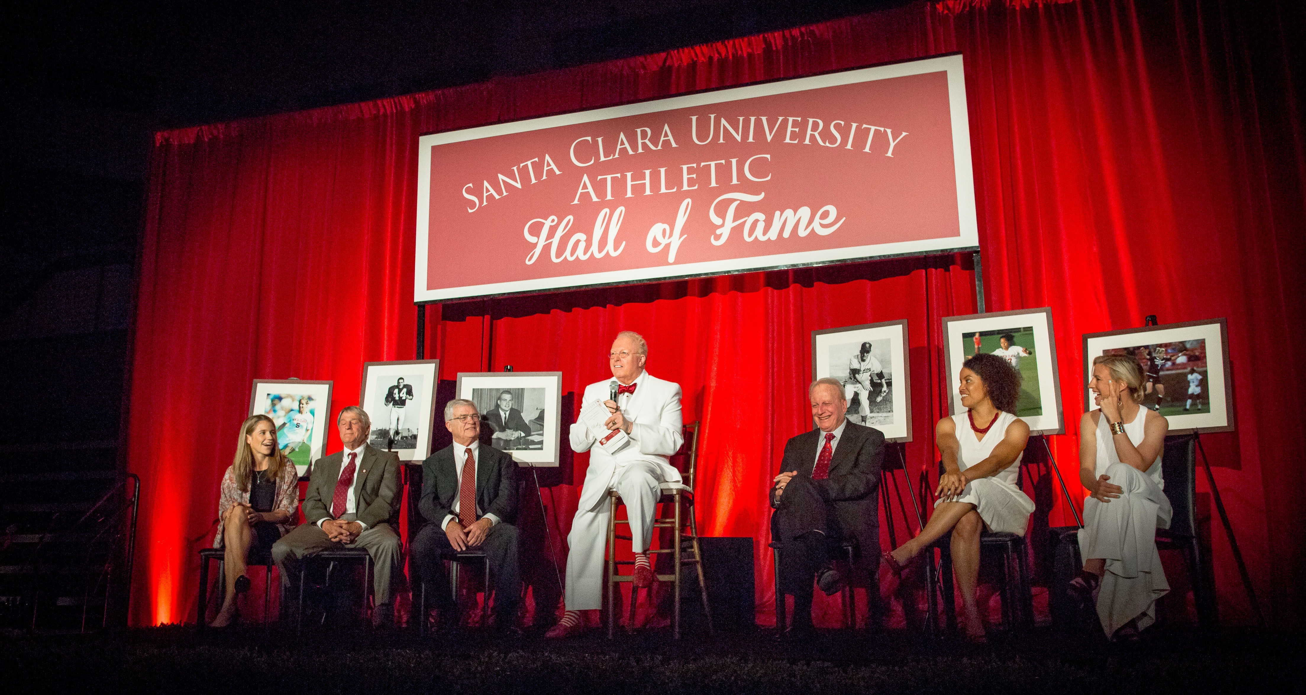 People on stage with a R + W 2014 banner behind them and framed photos on display.
