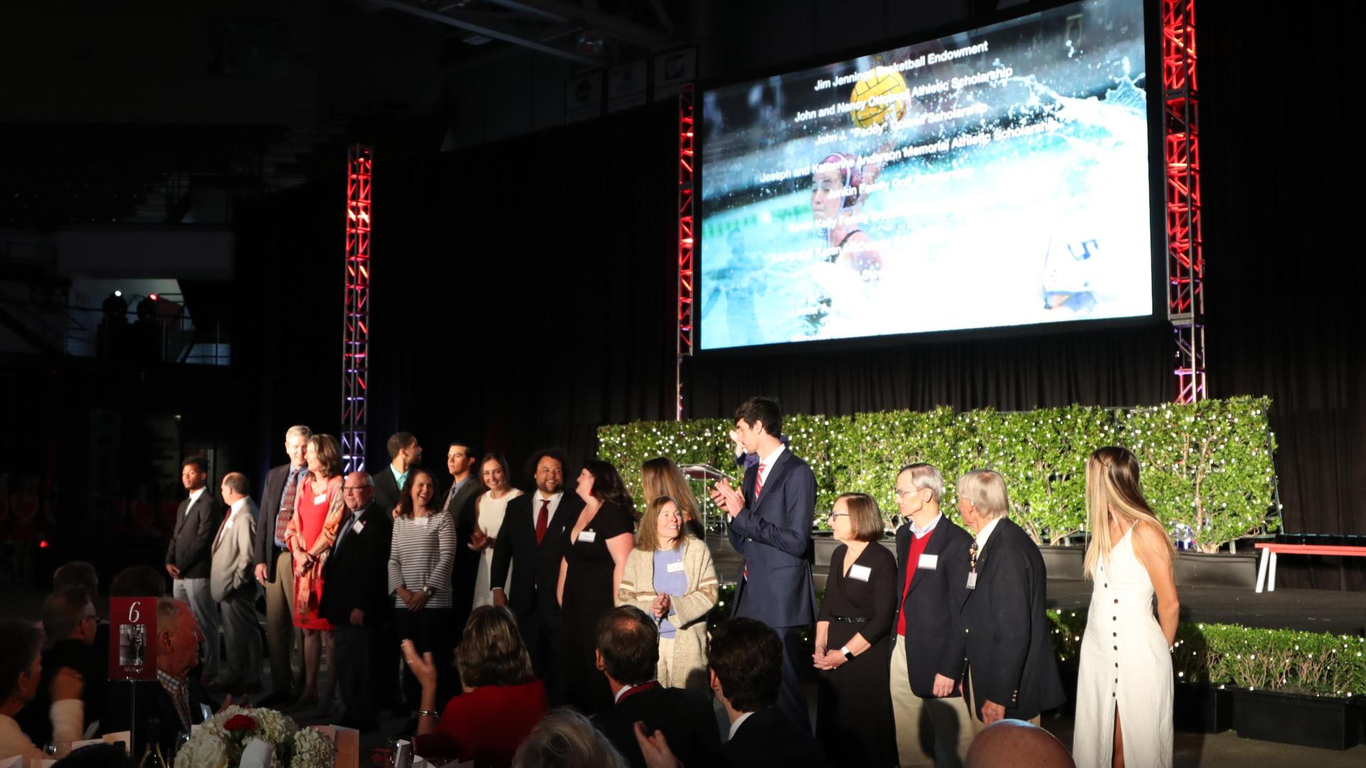 A group of people standing on a stage with a large screen behind them.