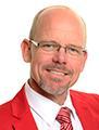 Man in a red jacket and tie, smiling.