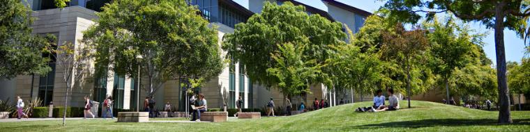 Students hanging out on campus on the grass and walking by.