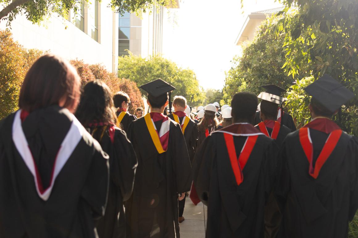 Graduates walking towards a sun drenched path.