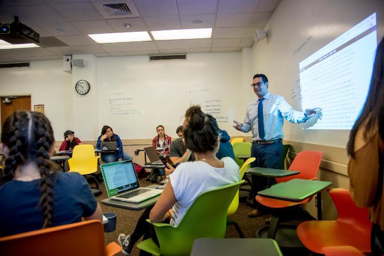 A person teaching in a classroom with students listening attentively.