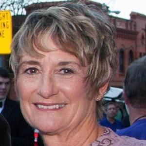A smiling person with short hair in a formal outfit outdoors.