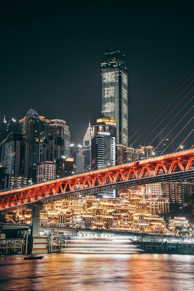 Chongqing, China; skyscraper city skyline at night with red, lit-up bridge in foreground