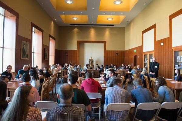 groups of students sit at several tables conversing in a large room