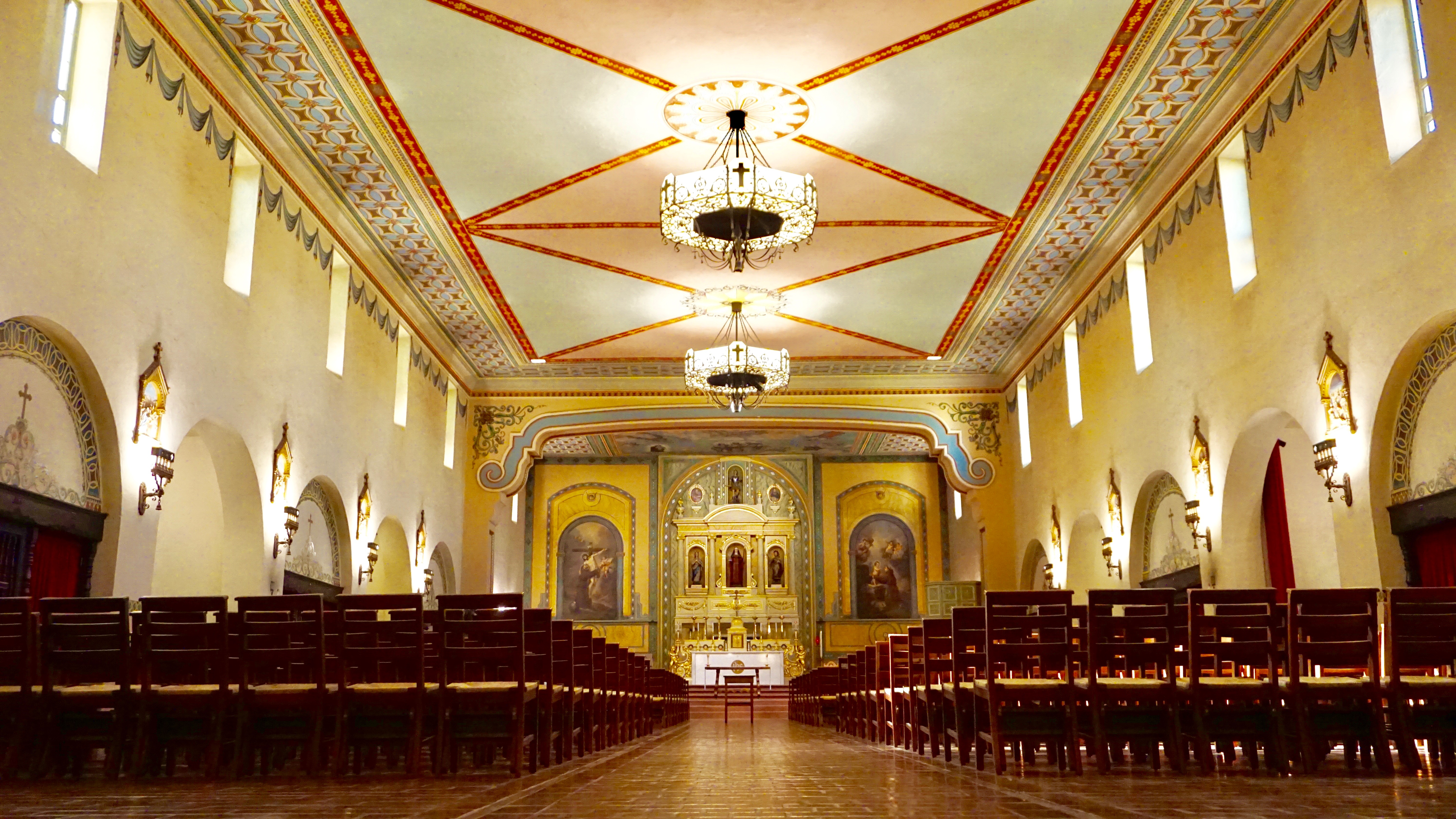 Wide-angle view of a mission church nave with wooden pews and ornate ceiling.