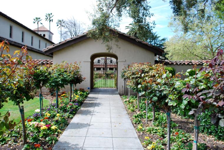 Pathway leading to Rose Garden Cemetery entrance framed by lush greenery and flowers.