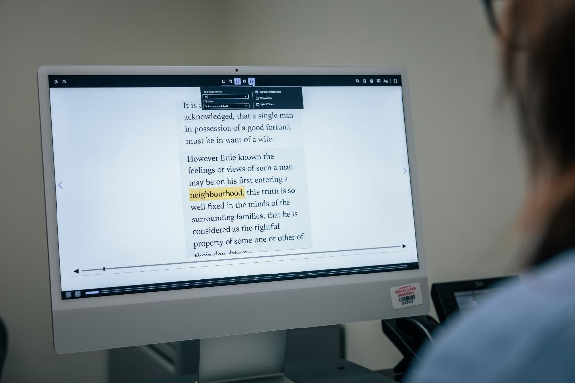 A person reads an ebook on a computer. The text is magnified and settings for text-to-speech are open.