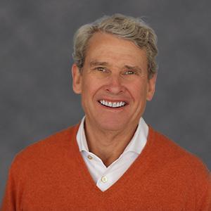 Head shot of man, smiling, with grey hair in red sweater and white shirt