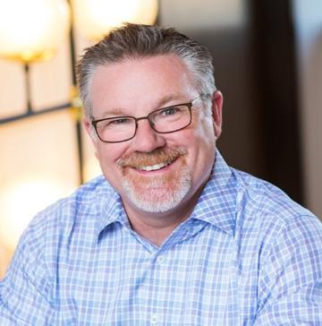 Image of man with short dark hair, grey beard and glasses in blue button-down shirt