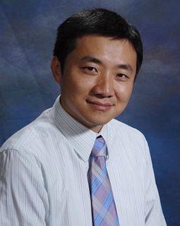 A person smiling, wearing a white shirt and tie against a blue background. image link to story