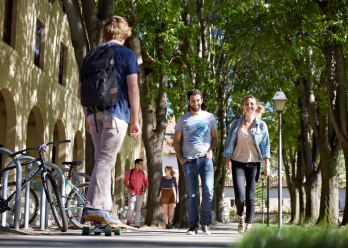 Student on skateboard and others walking through campus 