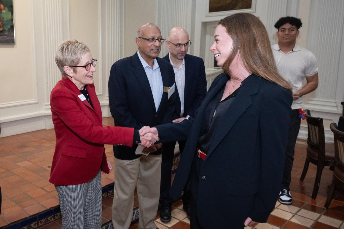 SCU student shaking hands with Julie Sullivan while two executives look on.