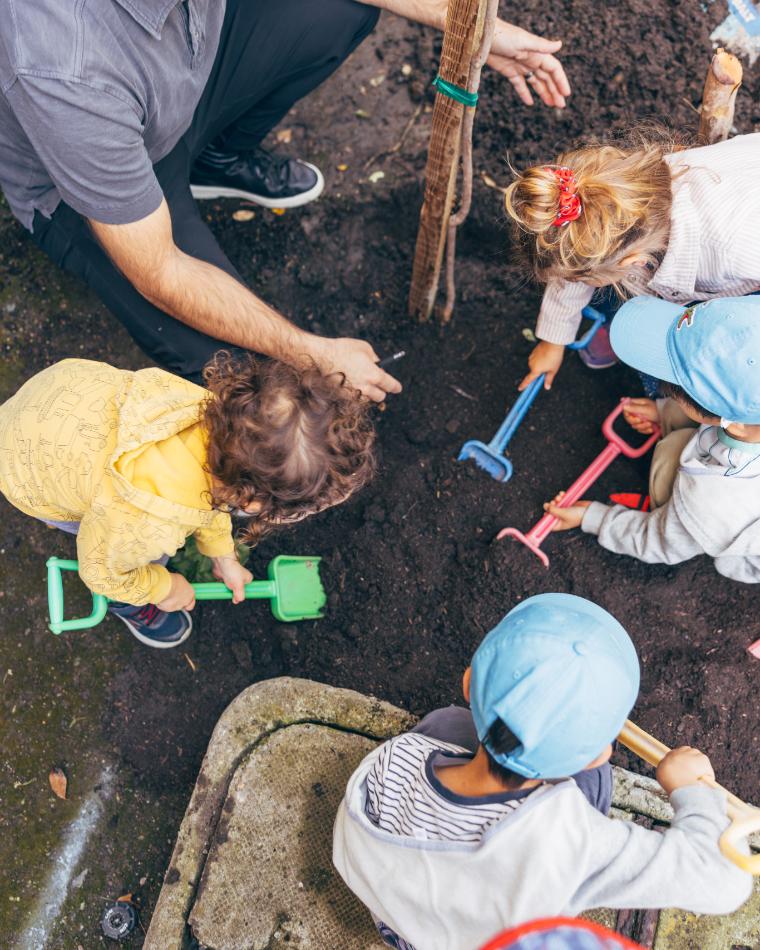 Arbor Day 2026: Group of KOC kids with plastic shovels plating a tree with a staff member