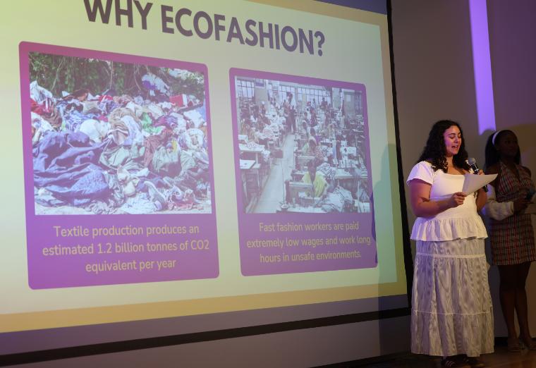 EcoFashion Show 2026: Student speaking on stage by a screen showing a slide titled Why EcoFashion