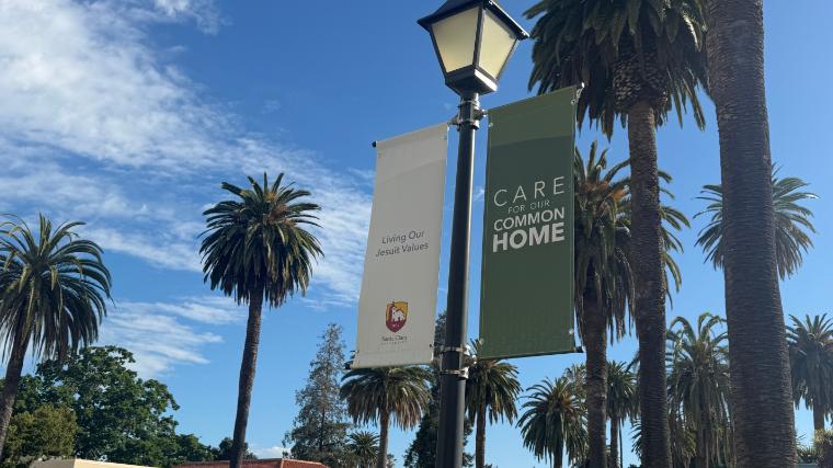 Light pole in front of palm trees with banners saying Care for Our Common Home and Living Our jesuits values