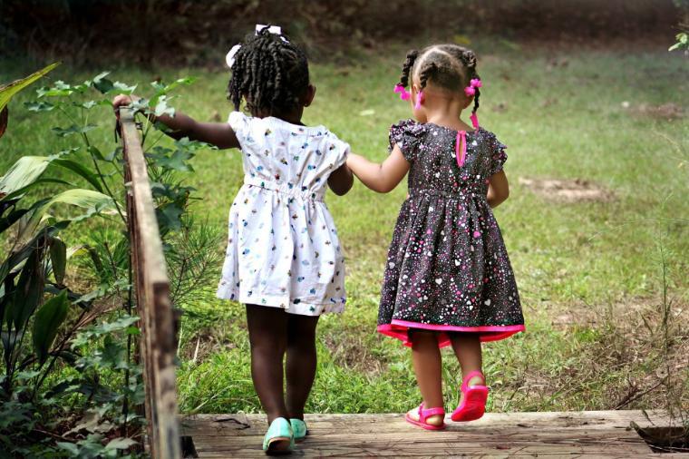 Two little girls walking on a grassy path holding hands.