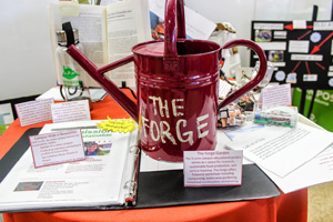 A red watering can with the text Smile, its spring on a table with various items. image link to story
