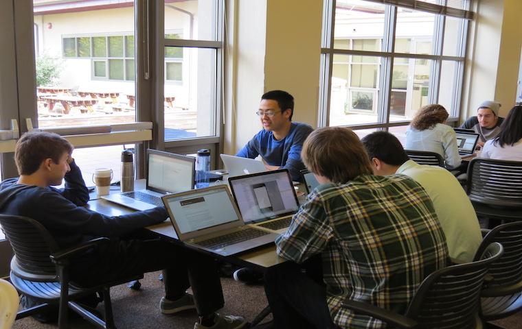 People working on laptops together in a room during a hackathon.