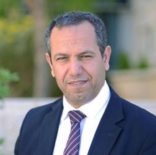 Man in a suit and tie standing outdoors, titled Salem Al-Agtash.