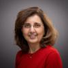 A woman in a red shirt smiles against a grey background. image link to story