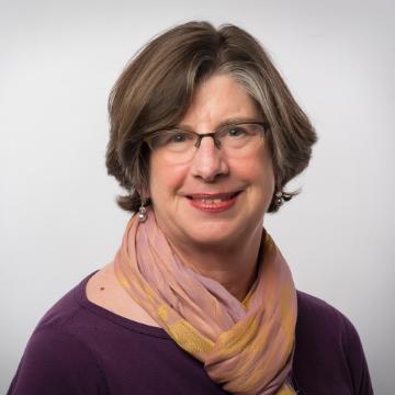 A person wearing glasses and a scarf, smiling at the camera. image link to story