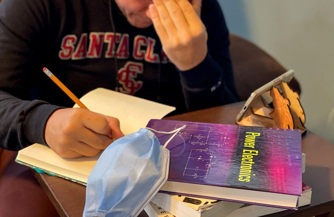 A stressed engineering student working at home with phone, mask, textbooks image link to story